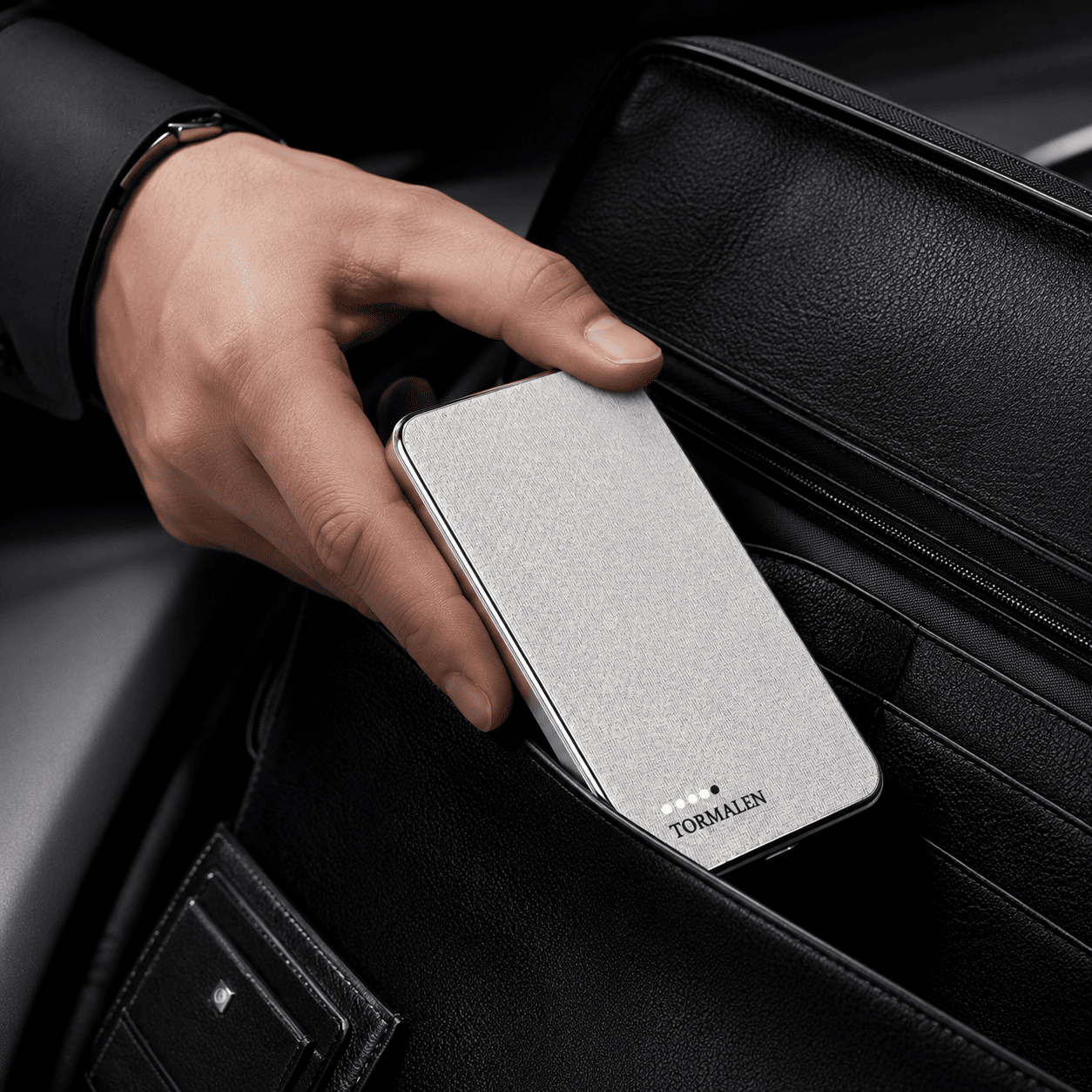 Hand placing a silver TORMALEN power bank into a bag